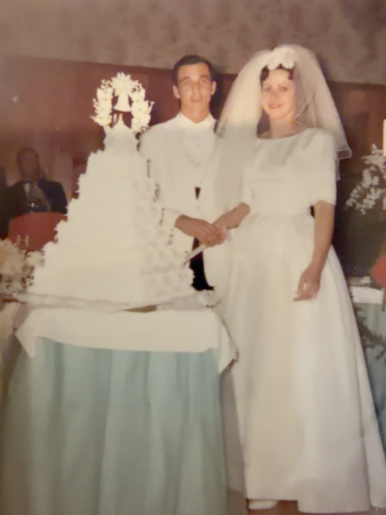 Carol Rudy Samuel and Bob Samuel standing beside their wedding cake.