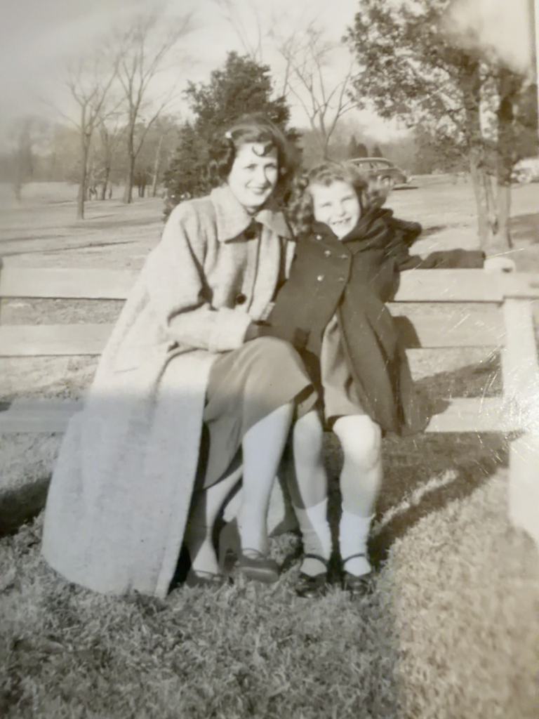 Anne Rudy Panella and Carol Rudy Samuel seated together on a park bench.