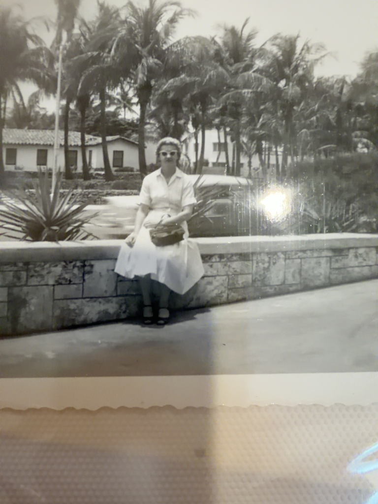 Viola Samuel seated beside a low wall, with palm trees behind.